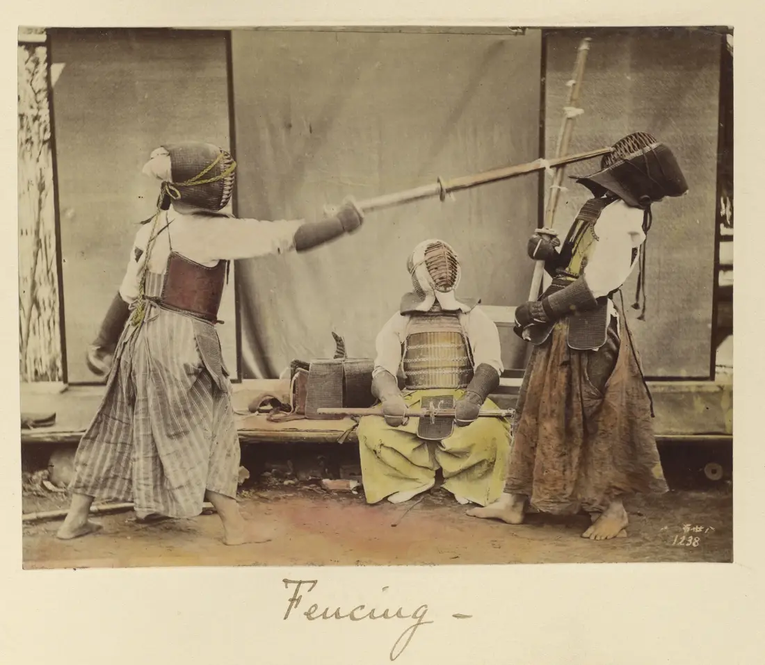 Two swordsmen in early kendo armour sparring with bamboo swords while a third watches, photographed in Japan in 1873